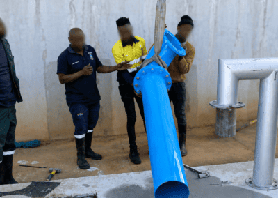 Workers guiding a blue pipe section over a concrete core hole at the Moloto reservoir project