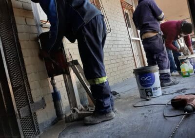 Team of core drilling technicians operating drilling equipment on a concrete structure during a building renovation project.