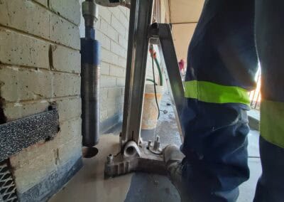 Worker operating core drill machine against wall to create concrete openings